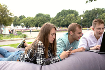 Three young friends relaxing outdoors in the park on a big cushion.