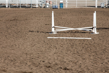 Single white horse jumping ring at a county fairgrounds with fallen rail