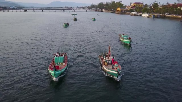 Drone shot flying low over traditional wooden fishing boats on the Prek Kampong river in Kampot, Cambodia.