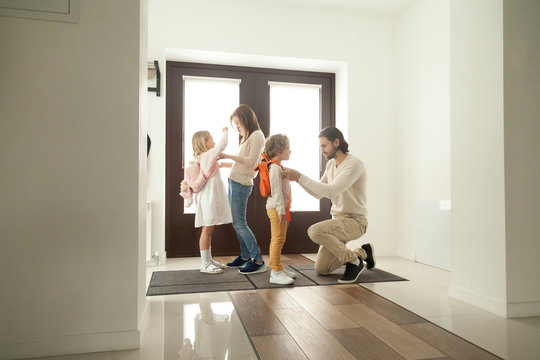 Parents get children ready for school standing at hallway, mother and father helping little preschool kids boy girl put backpacks on at home hall, mom with dad dressing son daughter in the morning