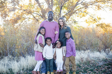 Beautiful bi-racial family portrait outdoors. Parents and their cute kids smiling and looking at the camera - Powered by Adobe