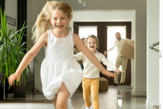 Excited children running on camera, funny little girl and boy having fun playing happy to move in new own big modern house, young family with kids and cardboard boxes entering home at moving day