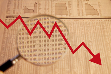Financial stock market analysis from newspapers business pages with red graph arrow pointing down – economy going downwards in fall