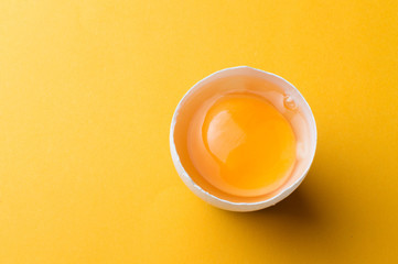 White egg and egg yolk on the yellow background. topview - obrazy, fototapety, plakaty