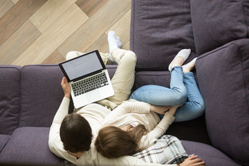 Young loving couple sitting on comfortable couch embracing holding laptop at home, man and woman...