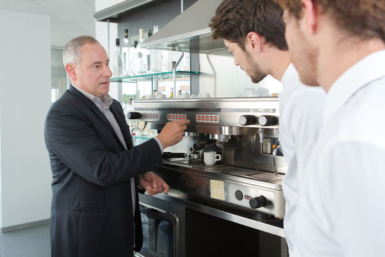 Manager teaching waiters how to use coffee machine