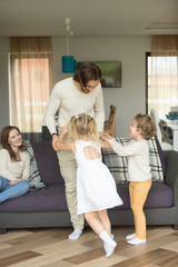 Young father playing with son and daughter at home, happy husband dad enjoys spending time with kids while wife mother sitting on sofa, little children love their daddy having fun together, vertical