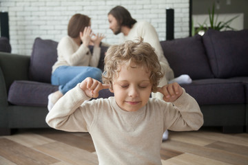 Fototapeta premium Little boy puts fingers in ears not to hear parents fighting at background, upset tired son suffering from mom and dad arguing, parental conflicts hurt kid, family divorce effect on children concept