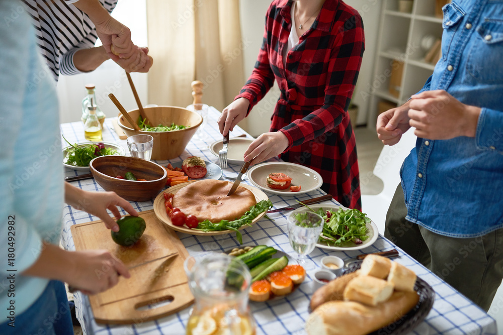 Wall mural Low section of unrecognizable people cutting pie and vegetables standing around dinner table with homemade food on it