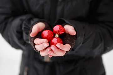 The frozen palm of a child standing in the cold and holding three red balls to decorate a Christmas tree