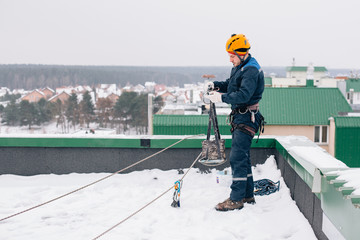 Industrial climber in uniform and helmet preparing to the work on the roof in winter