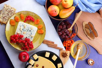 Cheese with mold, fruit, hard cheese with holes on a dark blue background, cheese on a black plate, fruits, nuts, honey, jam, Christmas dinner
