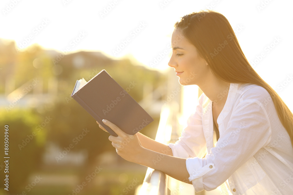 Wall mural woman reading a book in a balcony at sunset