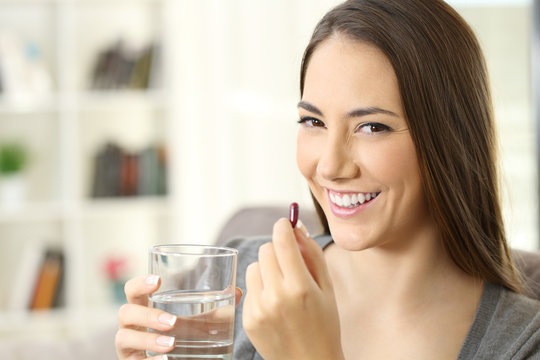 Happy woman looking at camera holding a pill