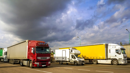 Colorful modern big semi-trucks and trailers of different makes and models stand in row on flat...