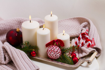 White burning advent candles with christmas decorations and knitted blanket