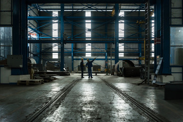 Two workers planning manufacturing process in the interior of an industrial hall