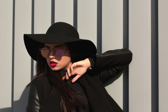 Lifestyle portrait of young woman in wide brimmed hat and mirror glasses posing near the shutters