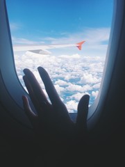 View from airplane window to sky and air plane wing, white clouds. Flight to vocation, woman hand...