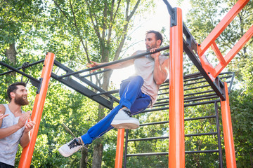 Low-angle view of a strong and determined young man doing amazing pull-up variation during extreme outdoor workout in the applauses of his friends