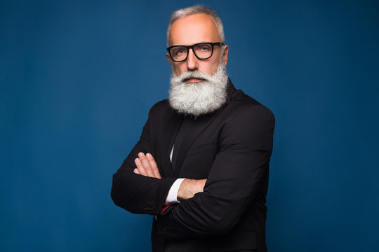 Close-up shot of handsome bearded man in fashion black glasses standing with arms folded isolated on a blue background
