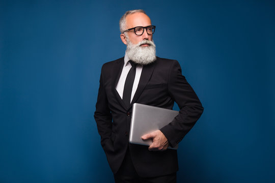 Concentrate bearded senior and business man staying with notebook and working isolated on a blue background. Working business man in straight suit and glasses