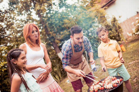 Happy young family barbecuing meat on the grill.