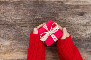 Christmas gift giving - someones hand in red knitted sweater holding red box with present