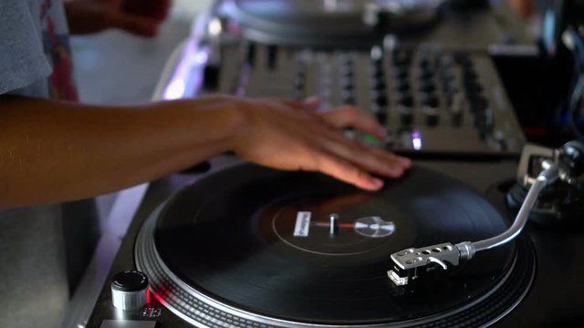 Mix and scratch, hands of a DJ on vinyl and mixer knobs. Slow motion 120 fps. Shooting with gimbal. Sunset.