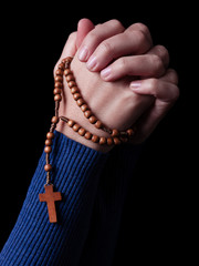 Female hands praying holding a rosary with Jesus Christ in the cross or Crucifix on black background. Woman with Christian Catholic religious faith