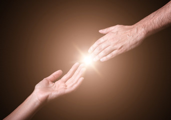 Reaching and touching hands. Bright light star flare with touching fingertips. Concept for salvation, rescue, friendship, guidance. Black background.