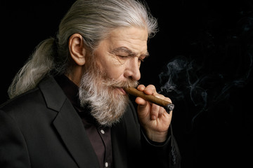 Side view of wrinkled stylish man with a cigar. Portrait of aged grey haired man smoking cigar.