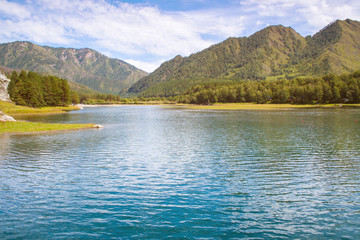 Fototapeta na wymiar A beautiful lake with mountains in the background. The magnificent scenery of the Altai mountains in Sunny weather. Reservoir Chemal hydroelectric power station