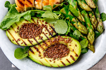 Healthy grilled chicken, grilled avocado and asparagus salad with linen seeds. Balanced lunch in bowl. Gray slate background. Top view