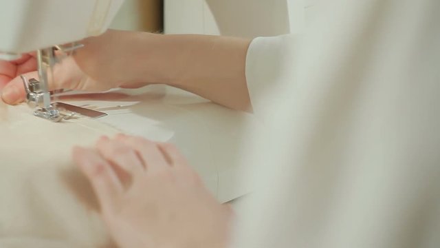 Closeup of a fashion designer woman sews on a sewing-machine an evening silk dress