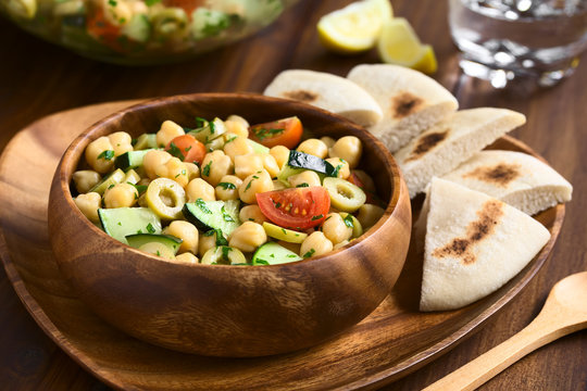 Salat aus Kichererbsen, grünen Oliven, Gurken, Kirschtomaten und Petersilie in Holzschüssel serviert, fotografiert mit natürlichem Licht (Selektiver Fokus, Fokus ein Drittel in den Salat)