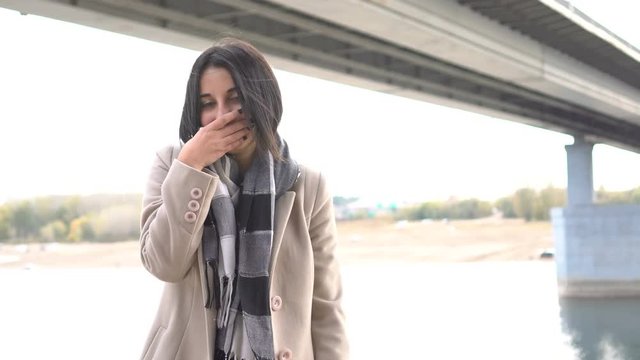 Girl coughs in park. Portrait brunette young woman. Girl is sick