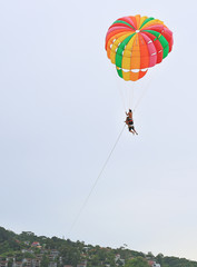 People are enjoy parasailing water sport. Fly with colorful parachute on the sky over the beach.
