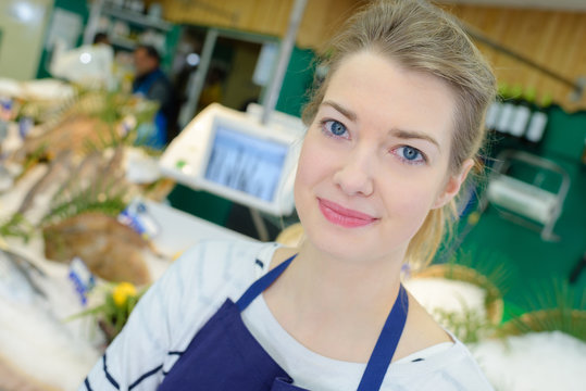 portrait of positive female shop assistant selling fresh fish