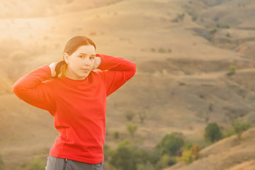 Fototapeta na wymiar The girl in the steppe mountains in a red fleece jacket and Hiking pants straightens hair tail in solar flare
