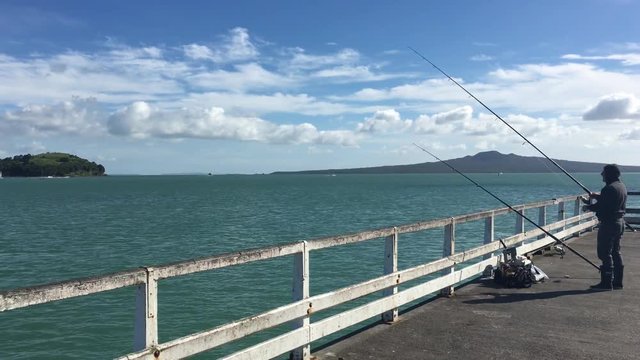 Unrecognizable fisherman fishing from Okahu bay wharf over Waitemata Harbour in Auckland, New Zealand.