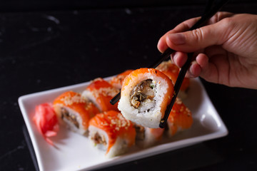 Japanese sushi rolls dish with hand holding one piece in chopsticks