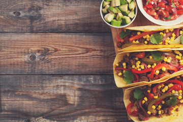 Three Mexican tacos with minced beef and mix vegetables on old rustic table. Mexican dish with sauces salsa in bowl and avocado. Spicy and hot street food. Top view with copy space