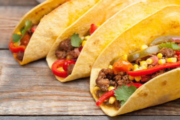 Three Mexican tacos with minced beef and mix vegetables on old rustic table. Mexican dish with sauces salsa in bowl and avocado. Spicy and hot street food. Close-up