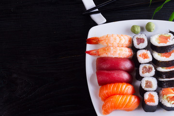 Japanese sushi dish on white plate with chopsticks on black wooden background closeup, top view