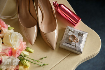 Wedding concept. Bridal accessories: wedding rings on ring box, bridal shoes on high heels, pink perfume bottle near wedding bouquet