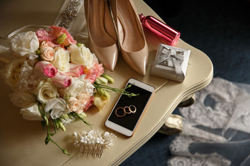 Wedding concept. Bride accessories: wedding rings on smart phone near ring box, bridal shoes on high heels, pink perfume bottle near wedding bouquet
