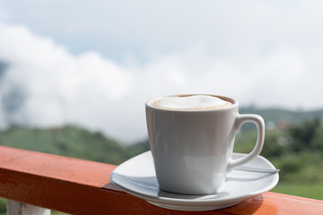 Close up white cup of hot coffee on balcony edge with outdoor natural green background