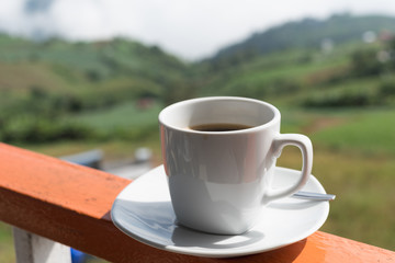 Close up white cup of hot coffee on balcony edge with outdoor natural green background