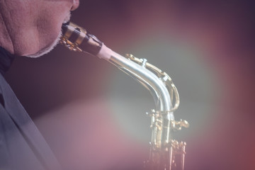 An elderly man plays a jazz melody on a saxophone. Tinted. Backlight. For music news or as a conceptual background.